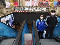Delivery worker for Alibaba's Hema Fresh wearing a face mask rides on an escalator behind a man at a shopping complex in Wuhan