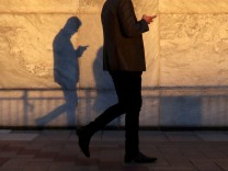 FILE PHOTO: An unidentified man using a smart phone walks through London's Canary Wharf financial district in the evening light in London