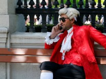 A concert ticket vendor dressed in a historic costume sits on a bench while making a phone call in Vienna, Austria