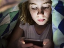 Ein Mädchen spielt unter der Bettdecke mit ihrem Smartphone