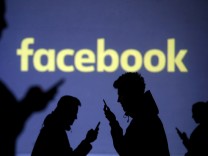 FILE PHOTO: Silhouettes of mobile users are seen next to a screen projection of Facebook logo in this picture illustration